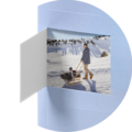A man pulls a friend on a sled through the snow. Snowy mountains and a blue sky are in the background. It's a cheerful winter day.