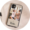 Two women laugh and enjoy a shared moment while holding a smartphone with a photo saying 'best mom'.